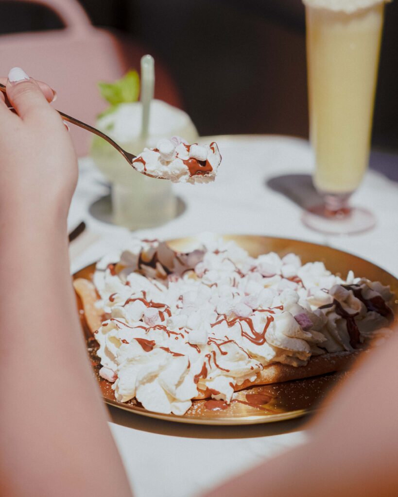 Crêpe Ballanger avec de la chantilly fait maison et des guimauves, posé sur une assiette en or, eux même poser sur une table en marbre.